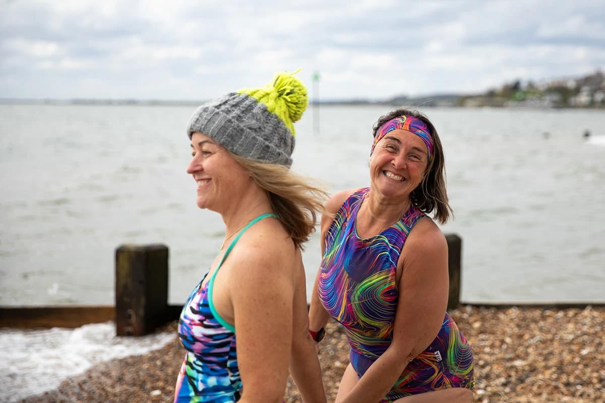Two friends laughing at the shoreline in colourful patterned swimsuits